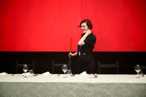 Louisa with a broom behind a table.