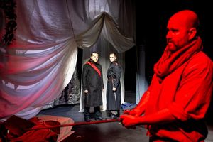 In the foreground Tristan holds a sword while two men watch from the distance.